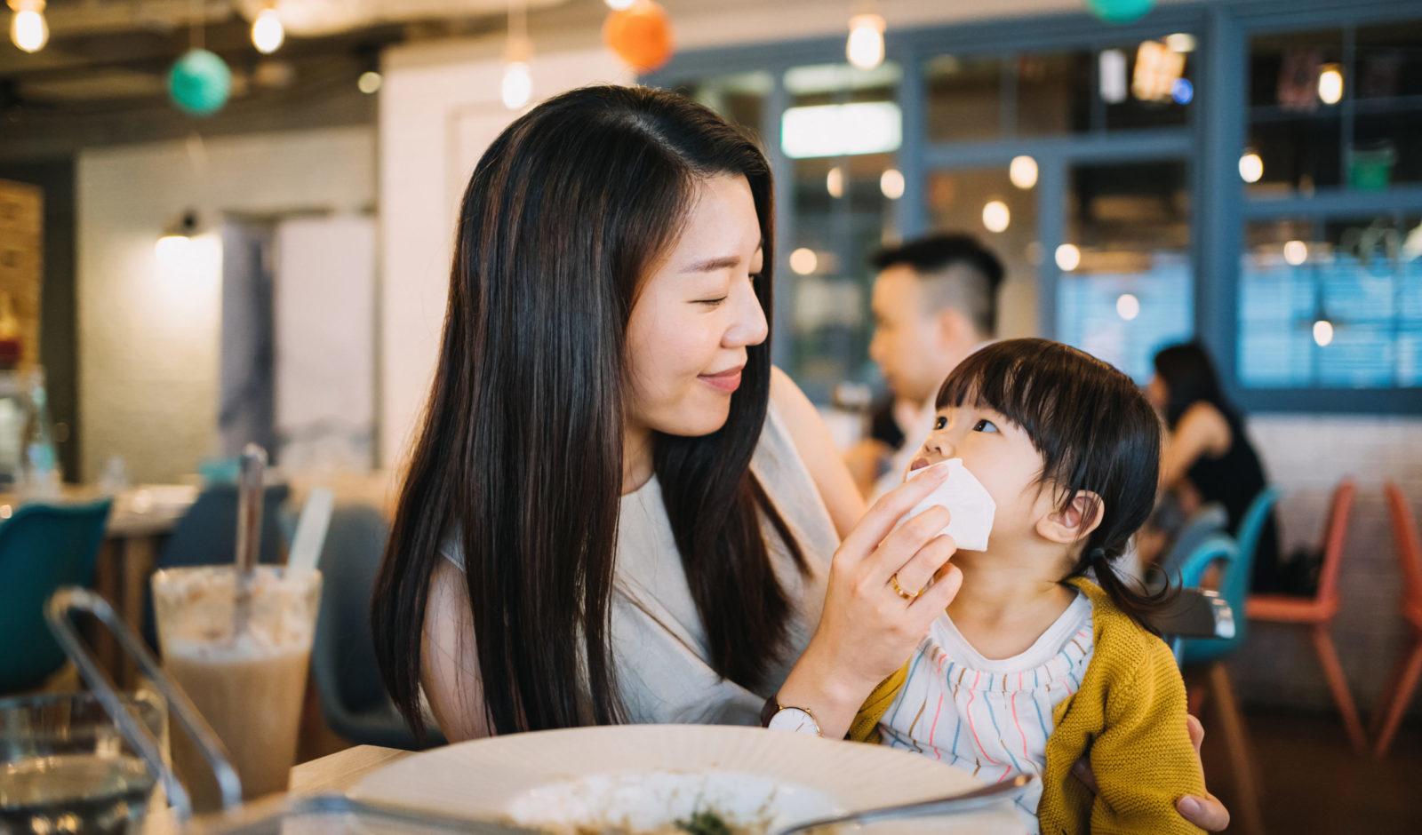 Caring young mother wiping daughter's mouth after meal in a restaurant